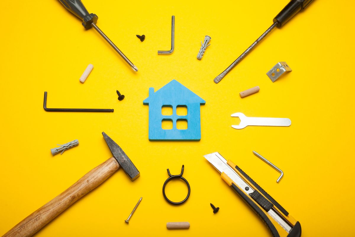 A collection of tools, including a hammer and wrench, in front of a house silhouette on a bright yellow background.